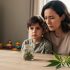 “Concerned parent sitting with a child at a kitchen table, with a sealed jar and cannabis leaves placed out of focus to suggest avoiding CBD and THCA for kids.”