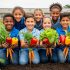 Students kneel in a school garden bed while harvesting fresh leafy greens and colorful vegetables together.